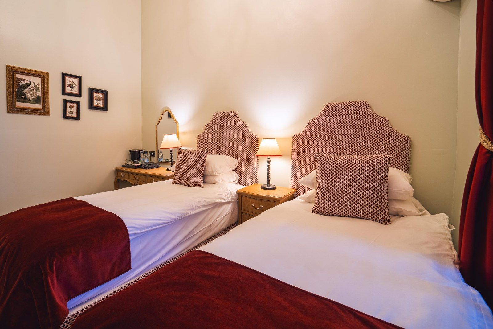 Two twin beds in a room with red and white striped headboards, lamps, and a small desk with a mirror.