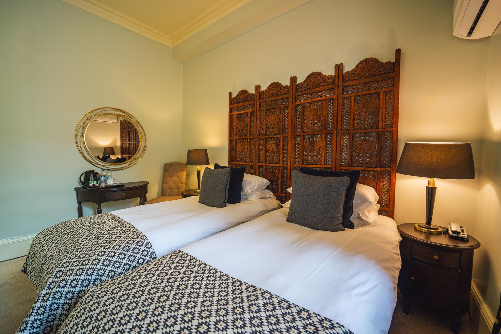 Twin beds in a bedroom with wooden headboard, side tables, mirror, and lamps.