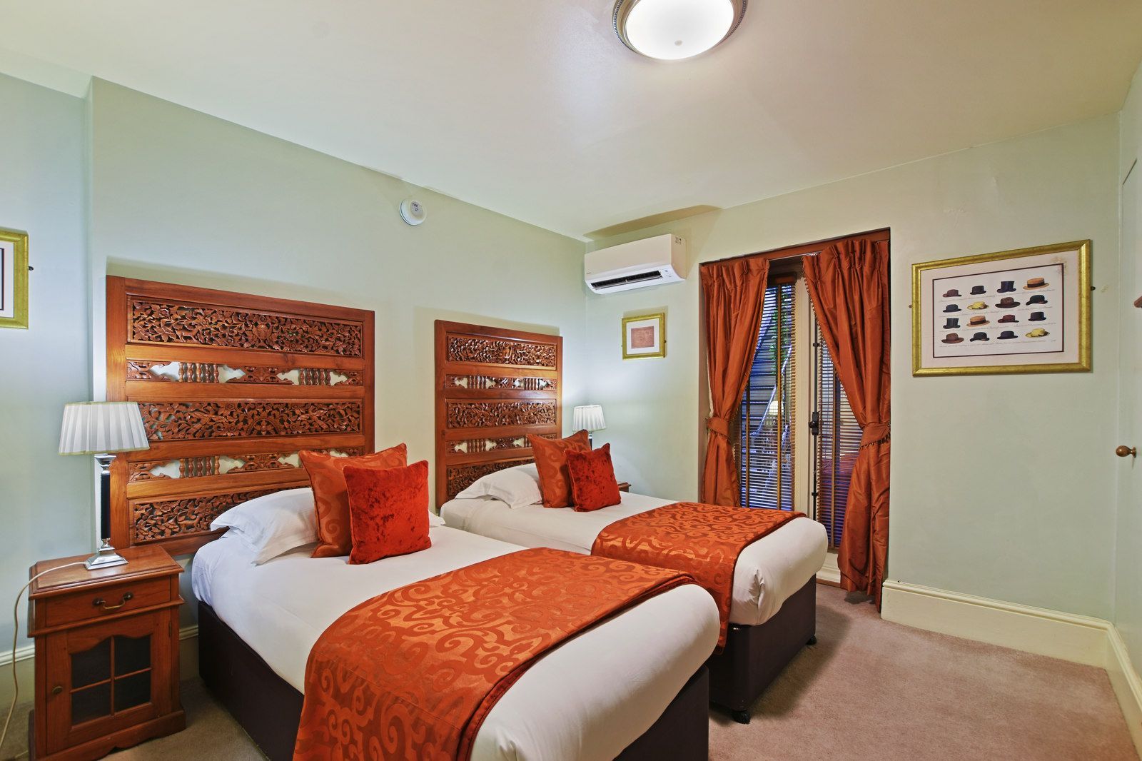 Twin bedroom with two beds, intricate wooden headboards, orange bedding, and a balcony.
