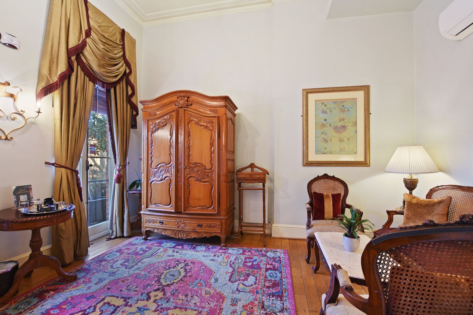 Room with wooden furniture, ornate rug, curtains, artwork, and French-style armoire.