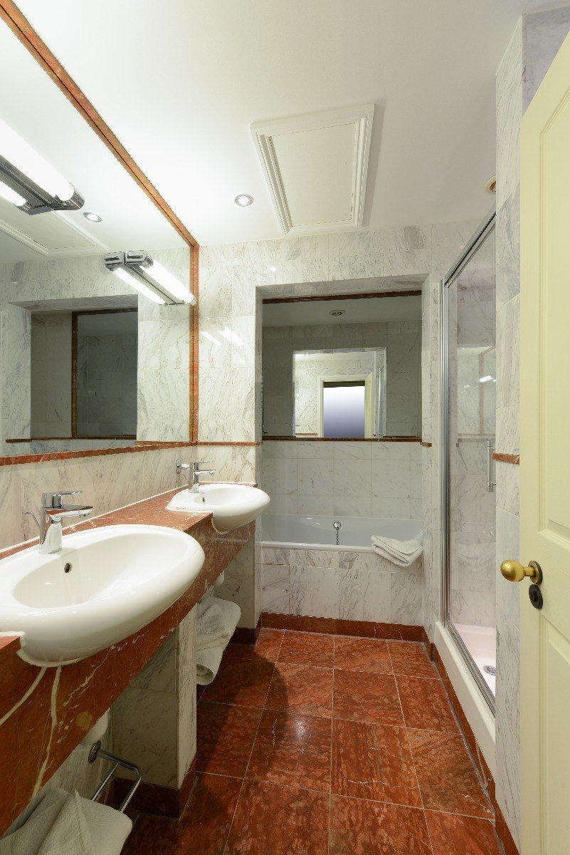 Bathroom with two sinks, a bathtub, and a glass shower. Red marble floor and counter, white walls and ceiling.