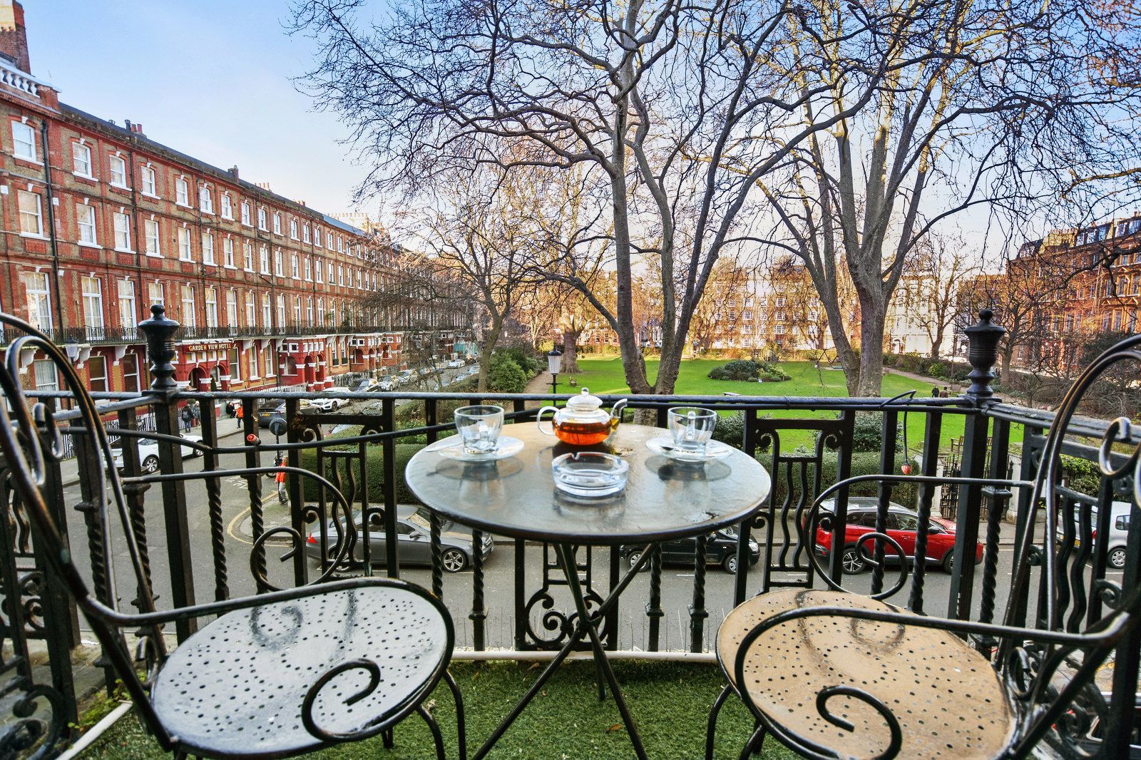 Balcony with table and chairs overlooking a park and buildings.