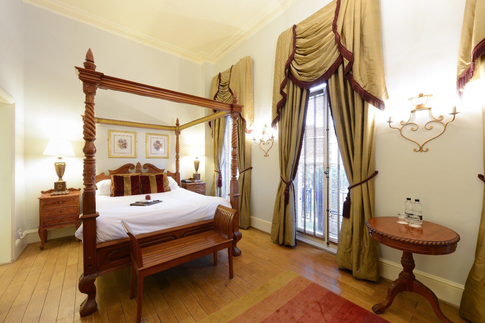 A luxurious bedroom with a four-poster bed, wood furnishings, and ornate window curtains.