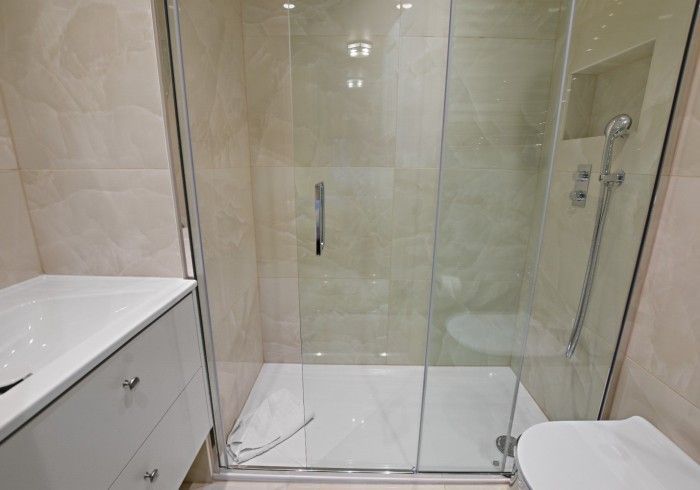 A modern bathroom with a glass shower, white vanity, and light-colored tile walls.