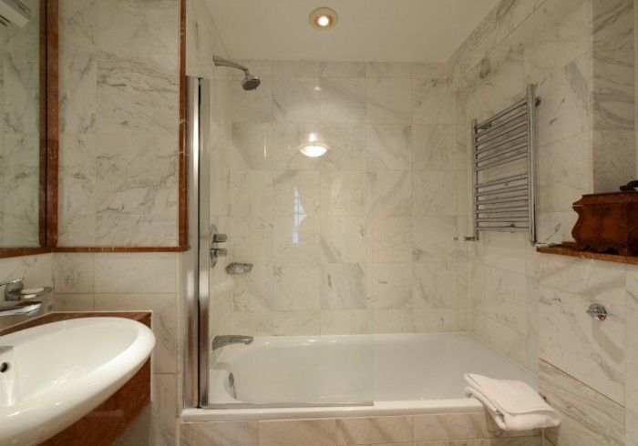 Bathroom with white marble walls, shower over tub, and heated towel rack.