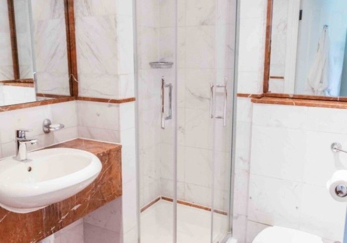 Bathroom with white marble walls, shower, sink, and toilet. Reddish-brown trim.