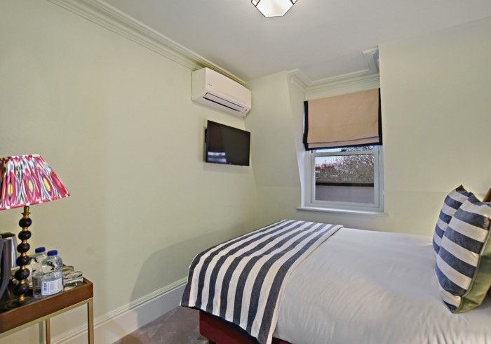 Small bedroom with a single bed, small window with a blind, and a wall-mounted TV.