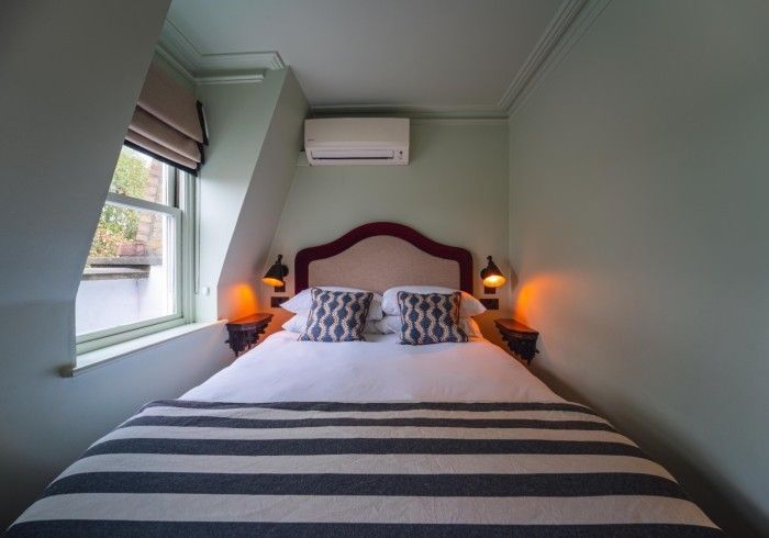 Bedroom with bed, striped cover, patterned pillows, window, and wall-mounted air conditioning.