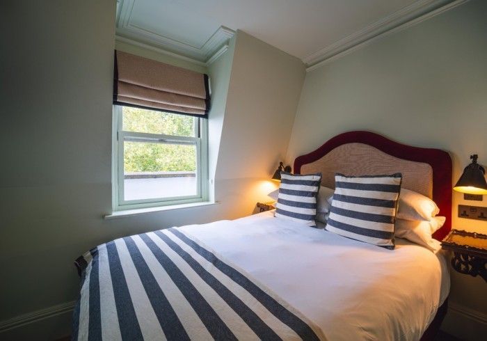 Bedroom with bed featuring striped blanket and pillows, window with shade.