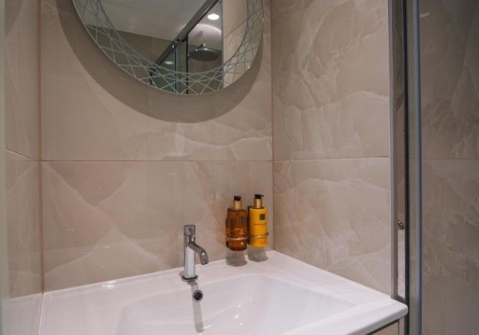 Bathroom with white sink, faucet, toiletries, and round mirror on beige tiled wall.
