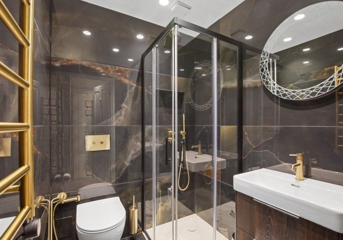 Luxurious dark bathroom with gold fixtures, shower, toilet, and sink.