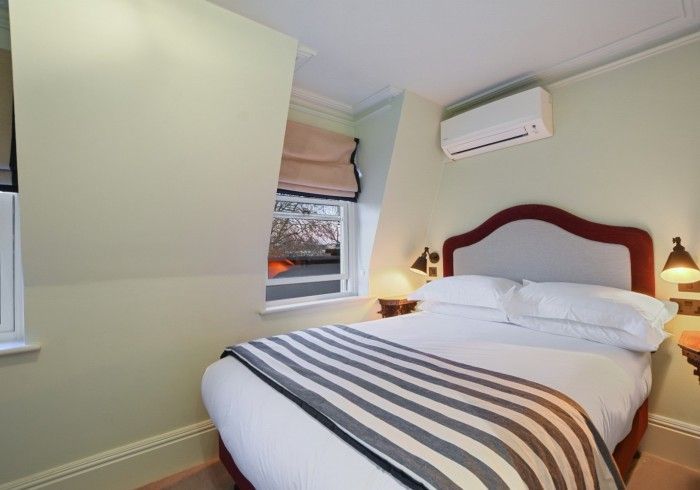 Bedroom with bed, window, and air conditioner; light green walls, white bedding, gray blanket.