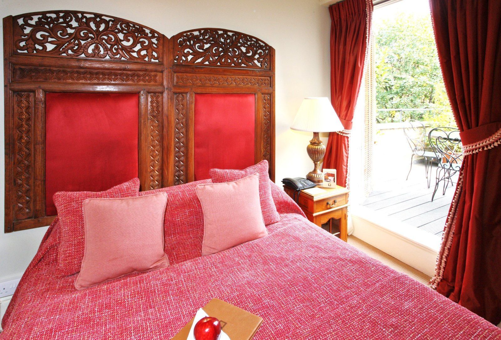 Bedroom with ornate wooden headboard, red bedding, and balcony access.