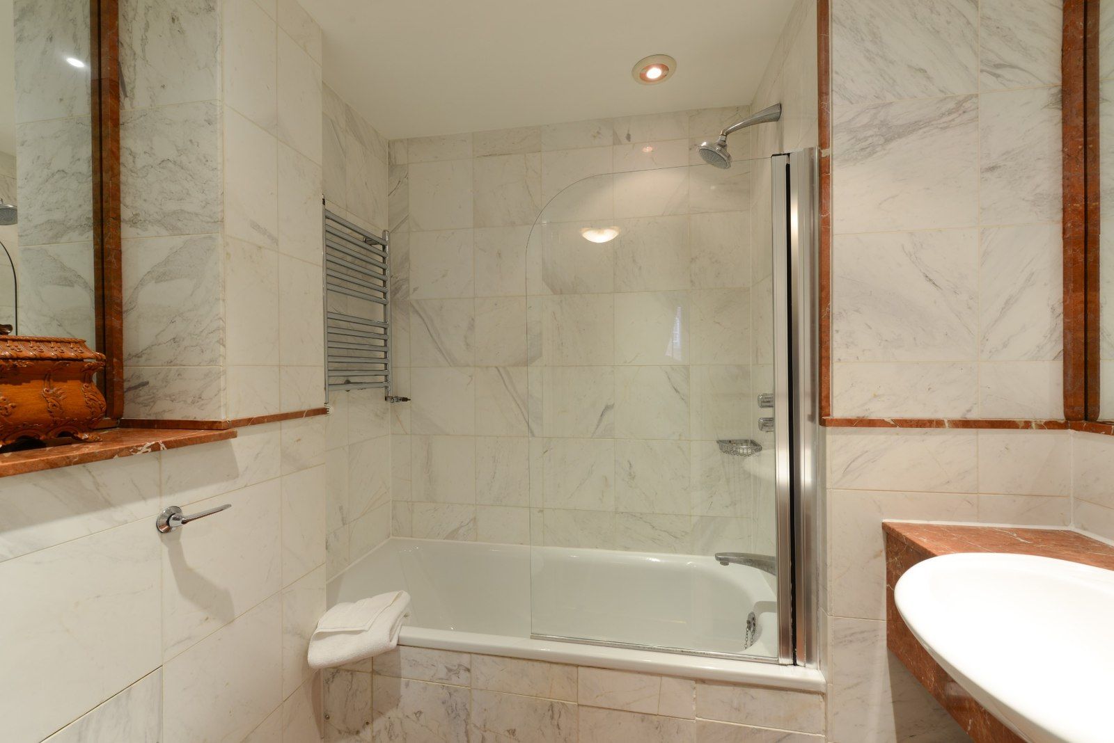 Bathroom with white marble walls, bathtub, and glass shower door.