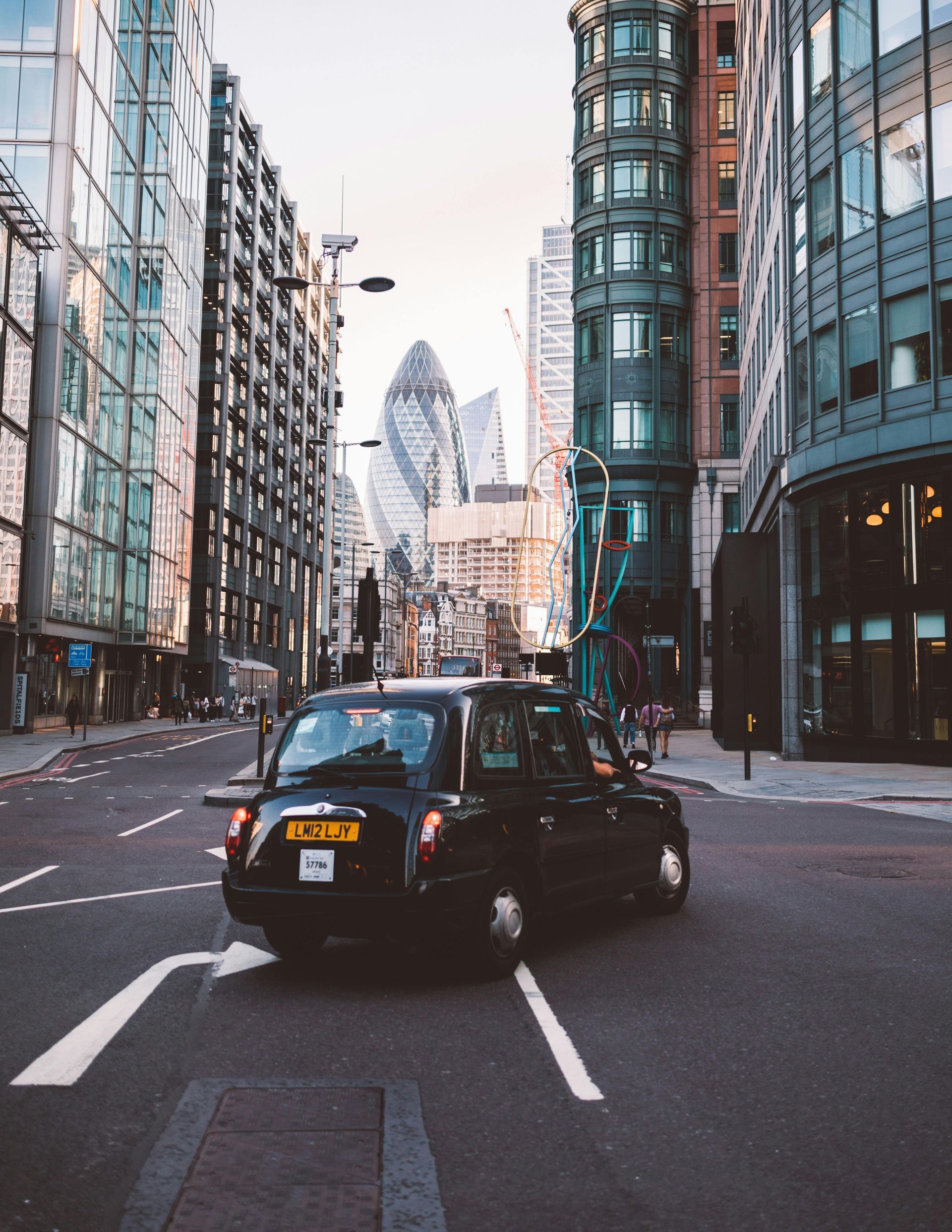 Black London taxi on a street in the city, surrounded by tall buildings, The Gherkin visible in the background.