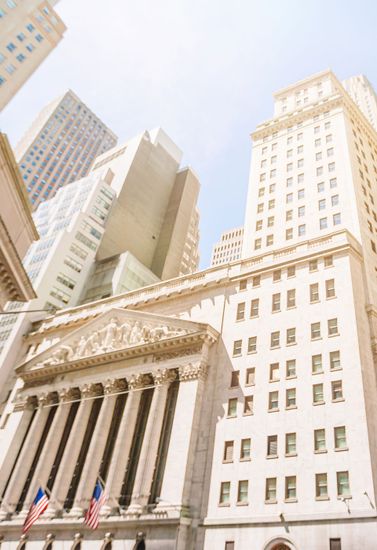 New York Stock Exchange facade with tall office buildings and American flags in daylight