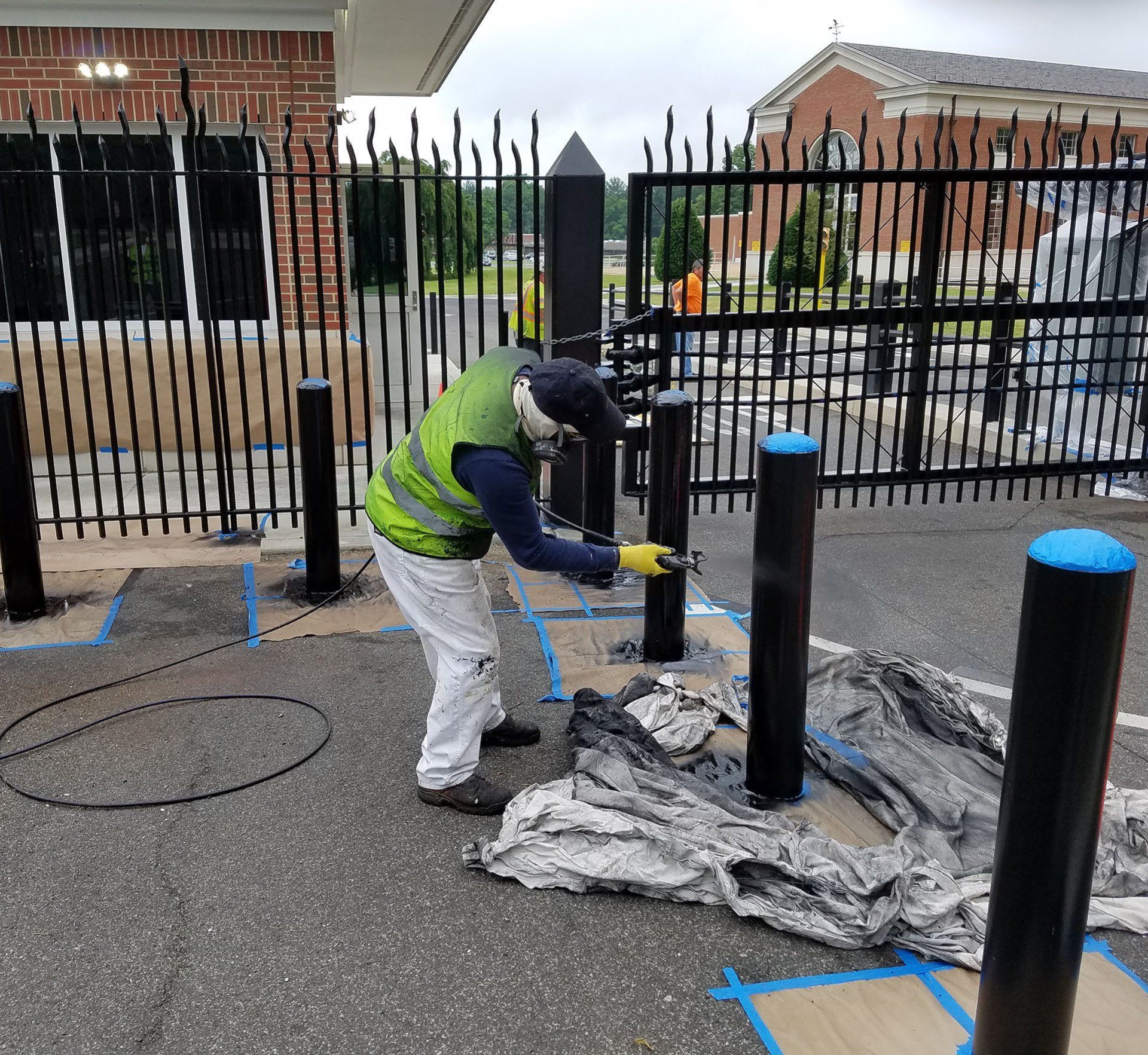 A man in a green vest is painting a fence post