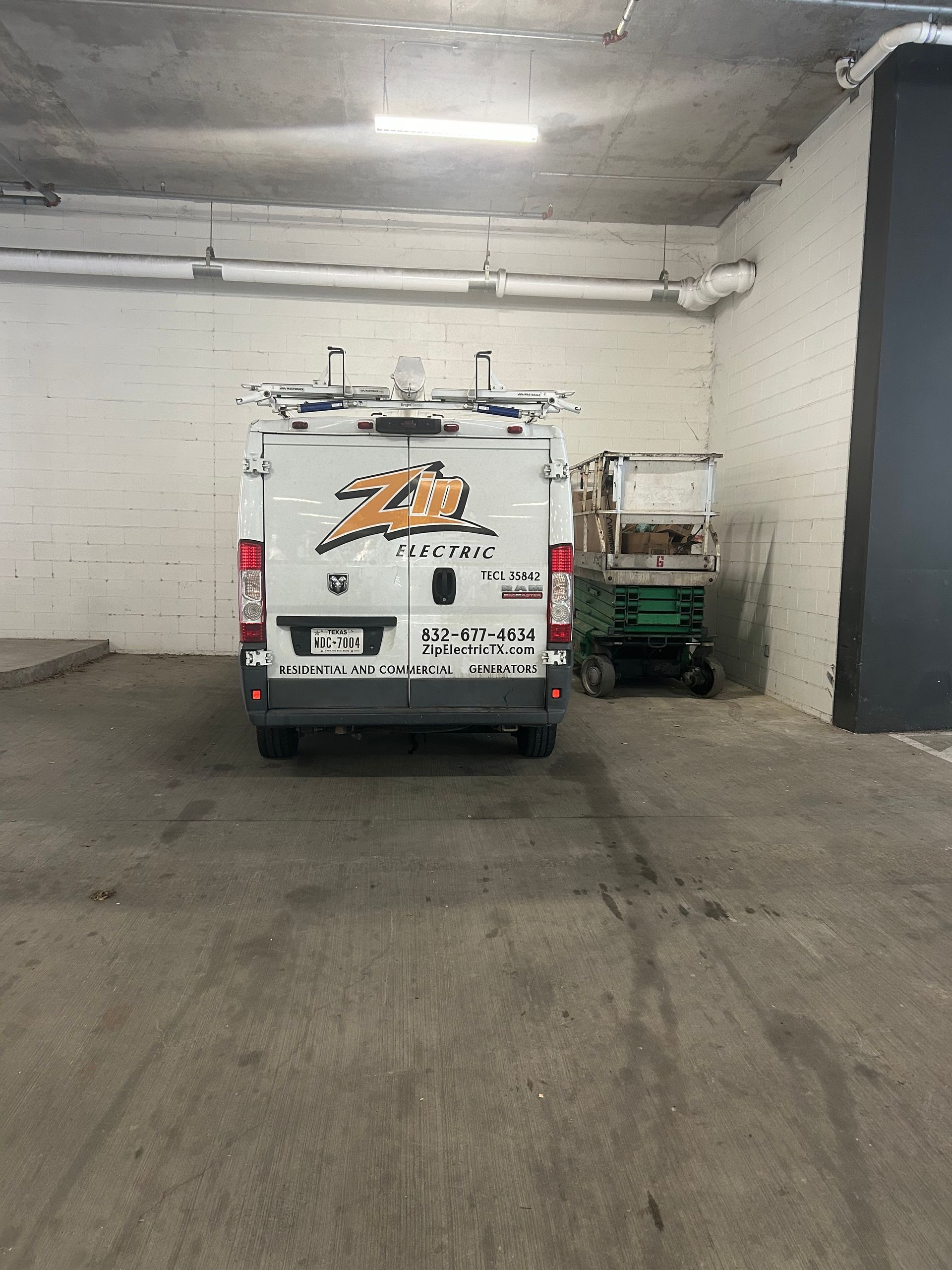 White utility van with logo in parking garage next to lift.