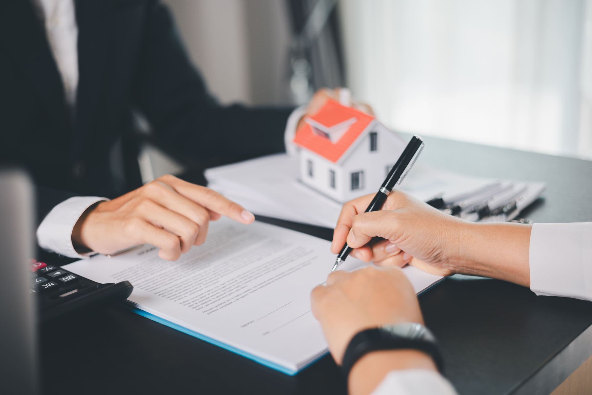 An estate lawyer is guiding a client on which documents to sign with a model house on the desk.