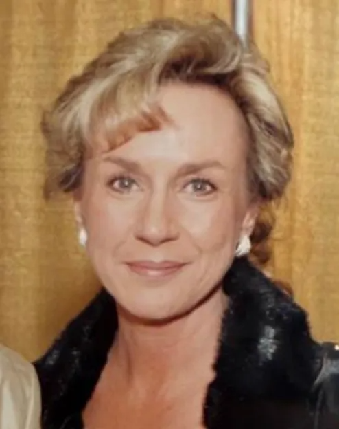 Portrait of a smiling woman in a black jacket against a gold curtain backdrop