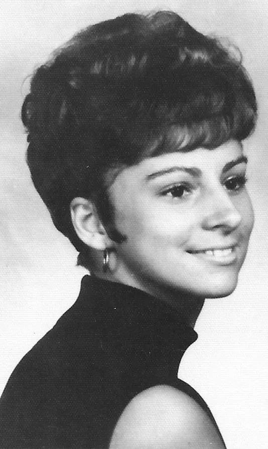 Black-and-white portrait of a smiling person in profile with a short hairstyle and dark turtleneck.