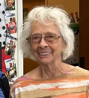 Smiling woman with white hair and glasses, wearing a striped shirt indoors.