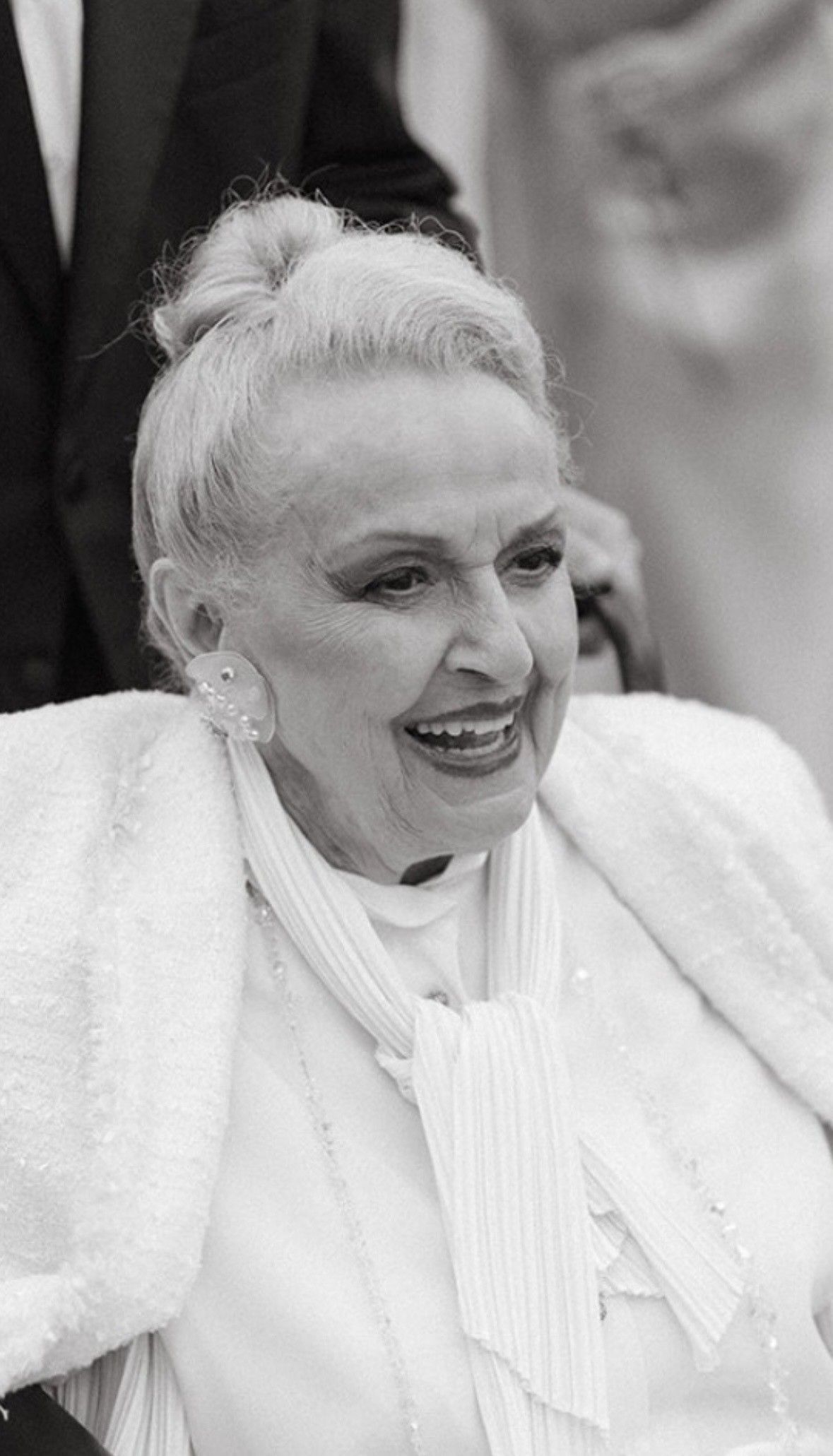 Smiling woman in a white outfit at a formal event, with an elegant updo.