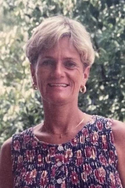 Smiling woman in a floral sleeveless top standing outdoors against leafy greenery
