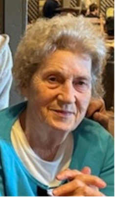 Elderly woman in a teal sweater smiling at a table indoors
