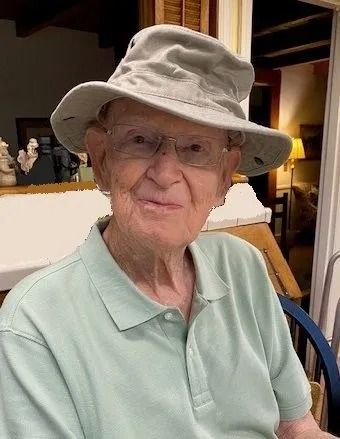 Older adult wearing a gray sun hat and light green polo shirt, smiling indoors at a table