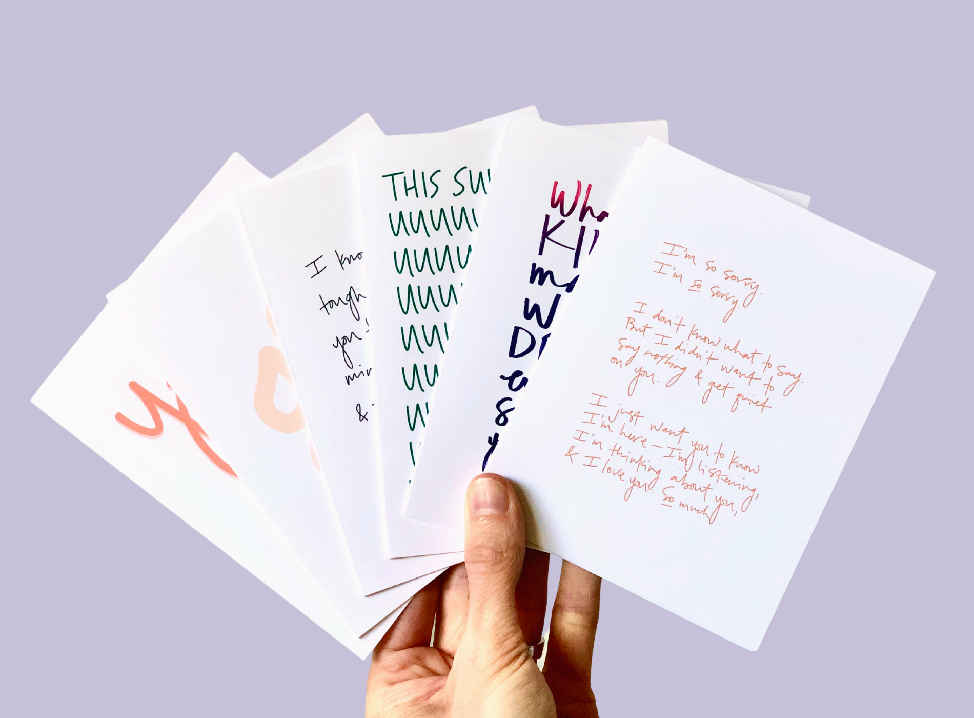 Hand holding a fan of white pages with handwritten notes in black, green, pink, and orange on a lavender background