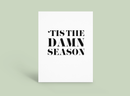 White poster with bold black text reading “’TIS THE DAMN SEASON” on a pale green background.