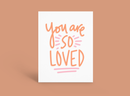 Handwritten “You are SO LOVED” on a white card with orange and pink lettering, on a peach background