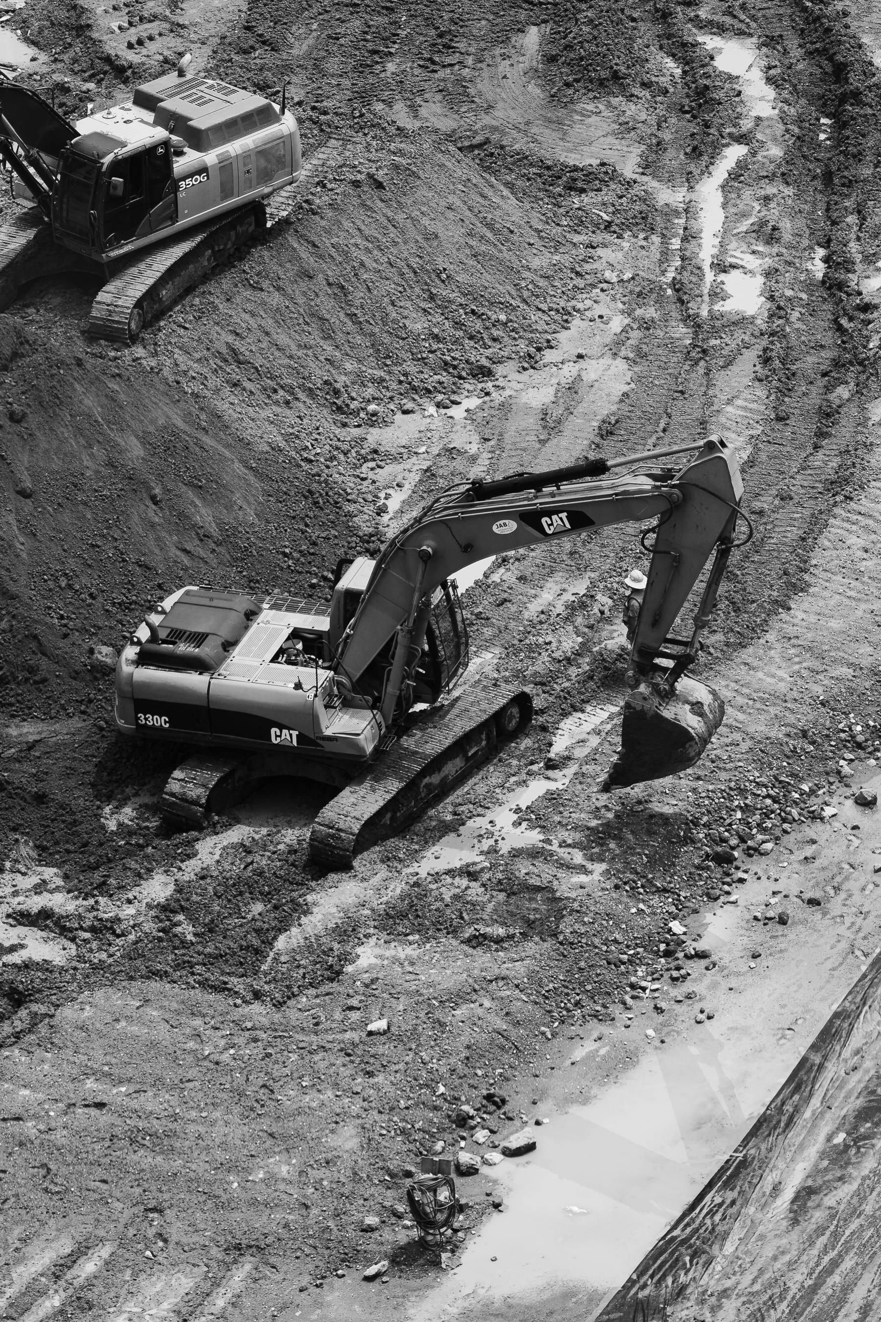 Two excavators on a dirt work site, one digging near a sloped concrete edge.