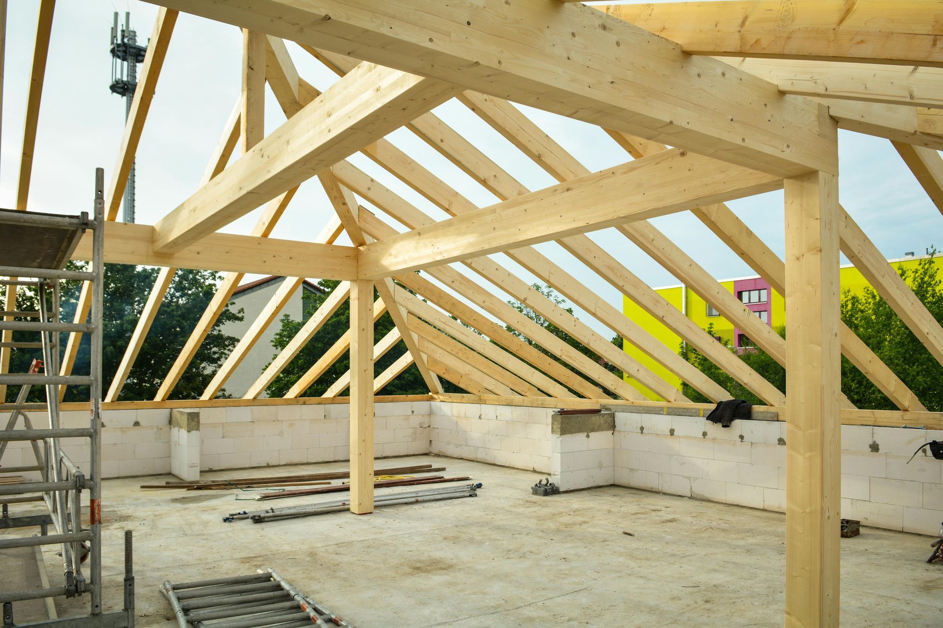 Wooden roof trusses under construction atop a building foundation, with scaffolding and open walls.