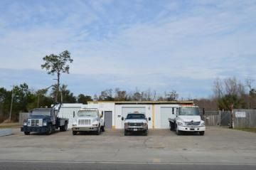 Four work trucks parked in front of a small warehouse under a cloudy sky