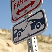 Road sign showing two tow trucks on a pole against a rocky desert background