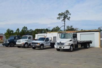 Several white trucks parked outside a warehouse on a concrete lot