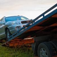 Silver car tilted on a car carrier trailer in a grassy roadside setting