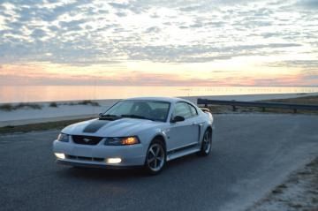 Silver sports car parked on a road at sunset near the water