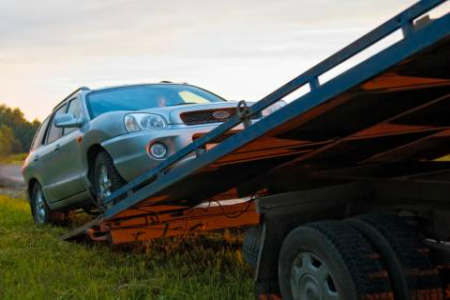 Silver car being loaded onto a blue tow truck ramp in a grassy field at sunset