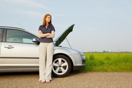 Woman standing beside a silver car with its hood open on a roadside