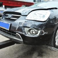 Damaged black car front bumper and headlight after collision, parked near a curb