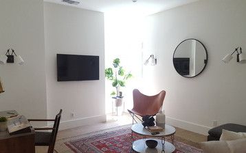 A living room with a chair , table , television and mirror.