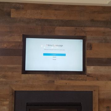 A flat screen tv is mounted on a wooden wall above a fireplace.