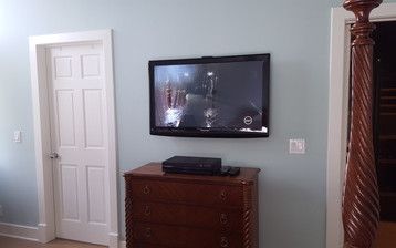 A bedroom with a television mounted on the wall above a dresser.