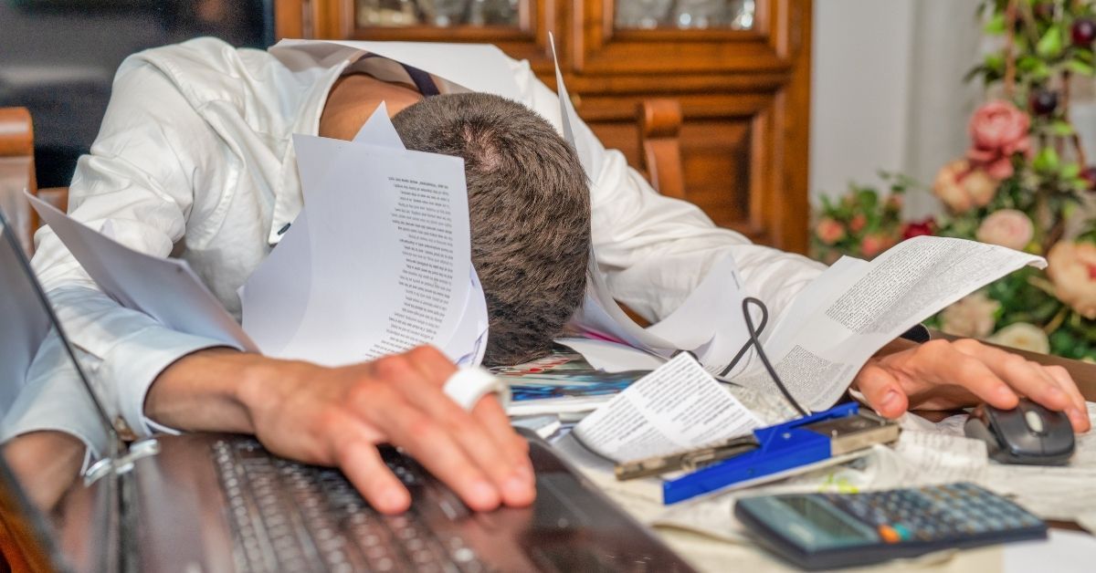 Overwhelmed business owner slumped over a desk covered in financial documents, representing the comp