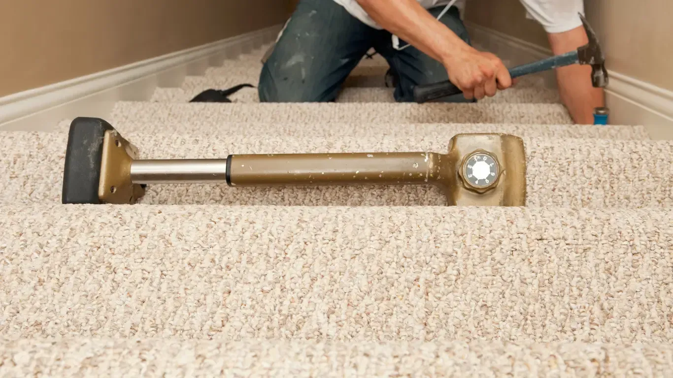 Carpeted stairwell with a worker installing a stair handrail.