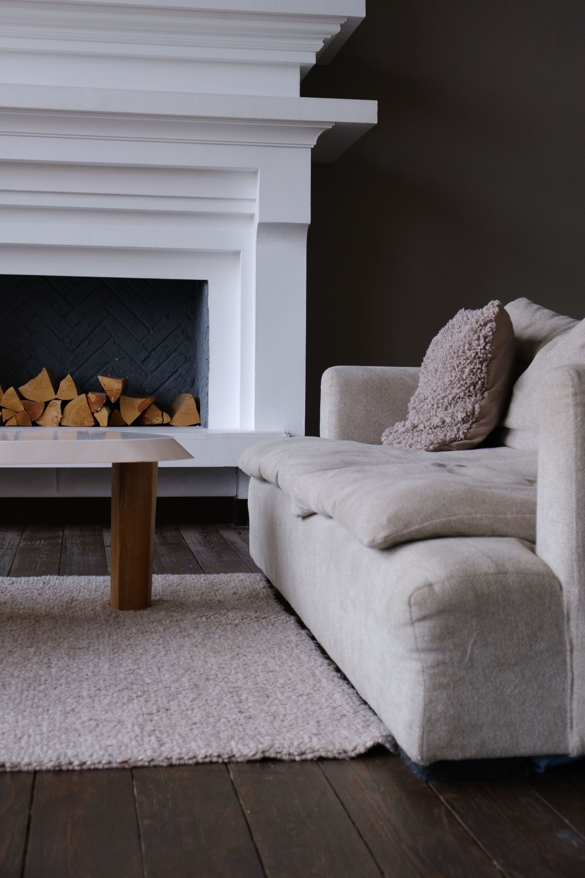 Cozy living room with a white fireplace, beige sofa, wooden coffee table, and gray rug