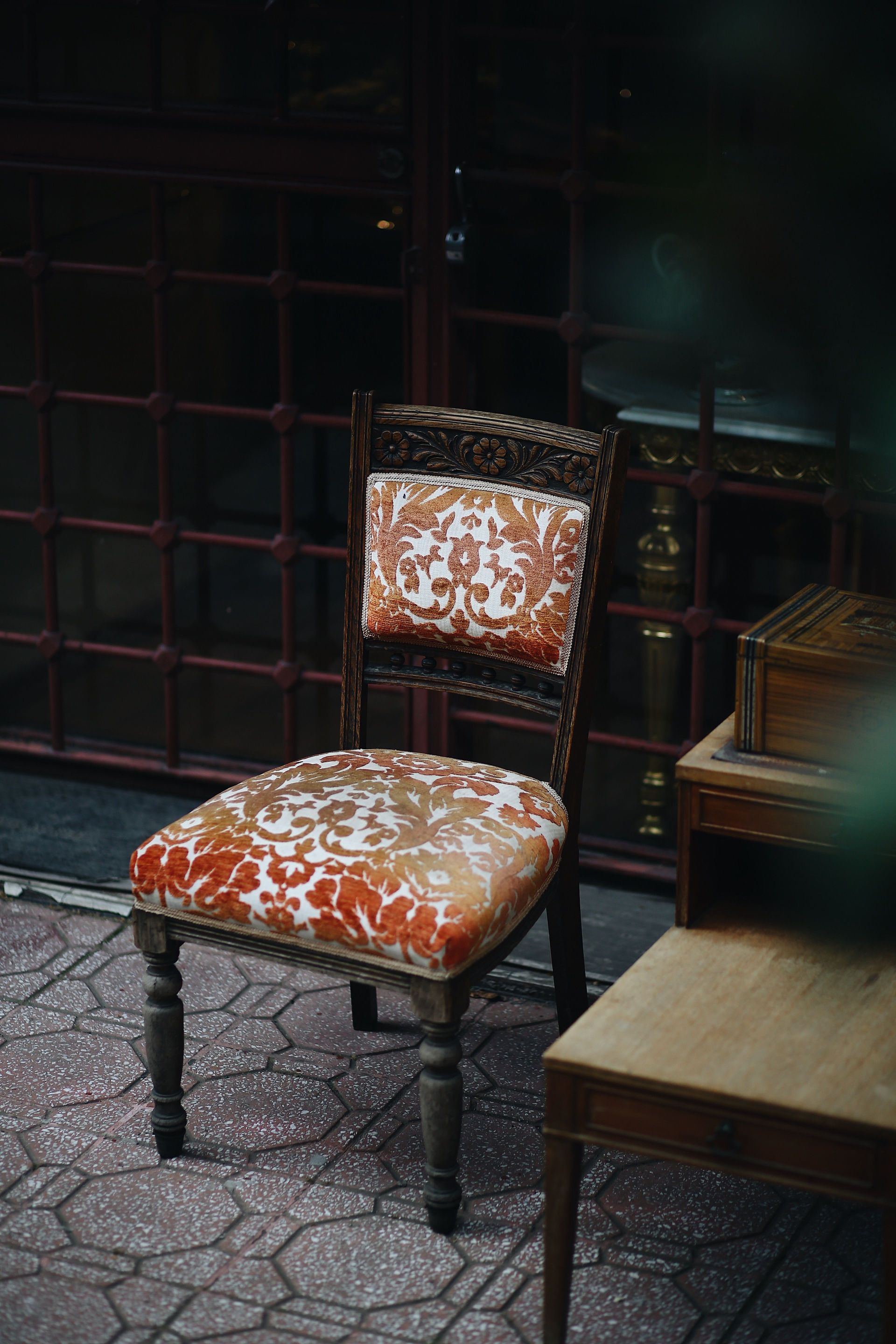 Ornate orange-and-white upholstered chair in a dim room with tables and a tiled floor